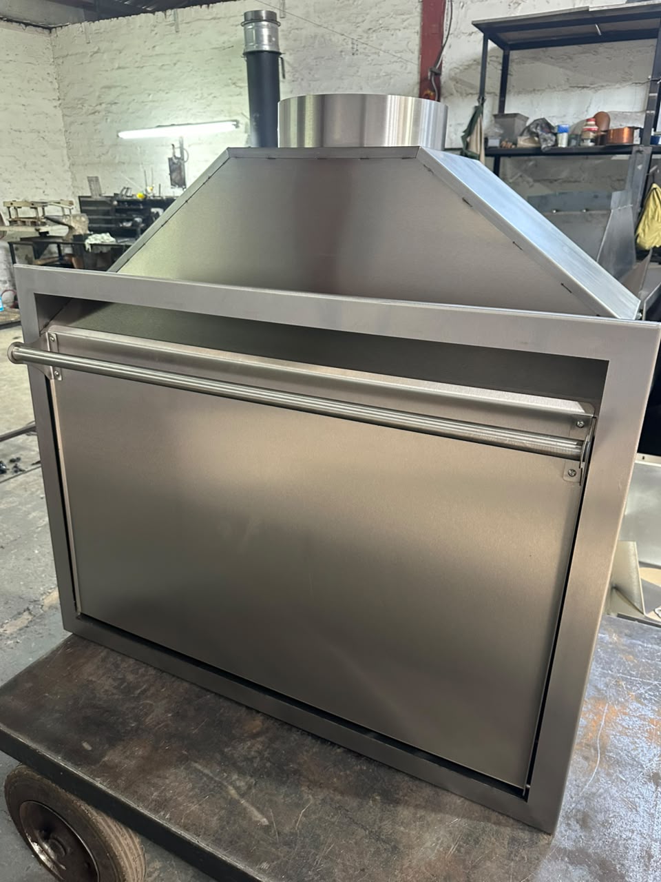 Angled view of a closed stainless steel built-in braai insert with a full-width door handle