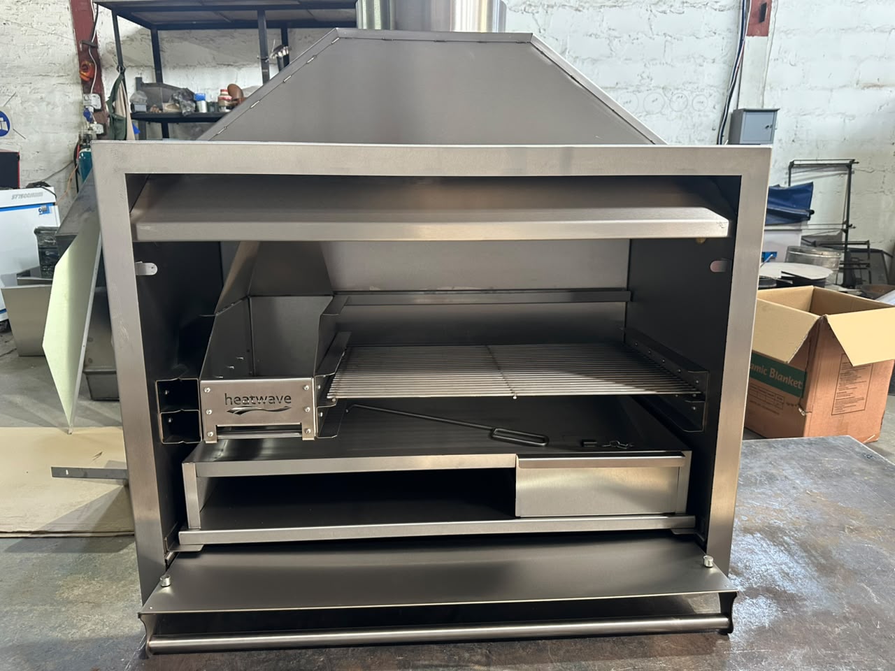 Open stainless steel braai with the fold-down door lowered and the cooking grid in place