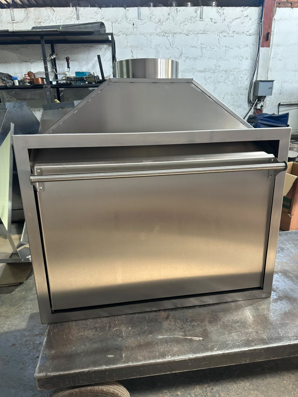 Front view of a closed stainless steel built-in braai insert with a tapered hood, chimney collar and fold-down door